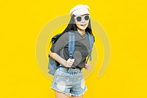 Traveler tourist young beautiful asian woman in hat and sunglasses with backpack,smiling and standing on yellow background.Summer