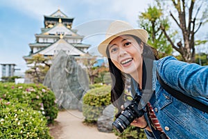 Traveler visiting osaka castle alone and taking selfie. young asian photographer holding digicam and having self portrait with