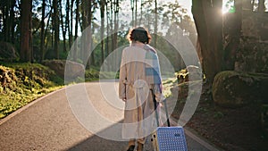 Traveler walking forest road with suitcase illuminated bright autumn sunlight.