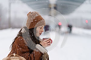 Traveler woman drinking hot tea travelling during cold winter waiting for train at outdoor platform