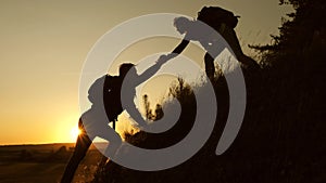 Traveler woman extends a hand to a man to a traveler climbing to the top of a hill. Tourists climb the mountain at