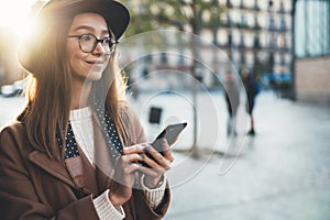 Traveler woman in hat hold in hands mobile phone. Smartphone technology internet connect online. Girl tourist in glasses using