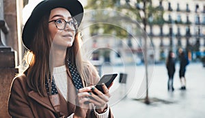 Traveler woman in hat hold in hands mobile phone. Smartphone technology internet online. Girl tourist in glasses using gadget