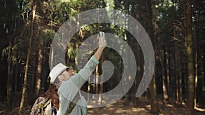 Traveler woman in a hat trying to catch a cell signal on the phone in the forest, no signal on the phone