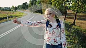 Traveler woman hitchhiking on a sunny road and walking.