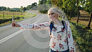 Traveler woman hitchhiking on a sunny road and walking.