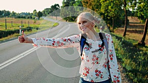 Traveler woman hitchhiking on a sunny road and walking.