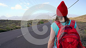 Traveler woman hitchhiking on a sunny road and walking. Backpacker woman looking for a ride to start a journey on a