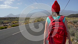 Traveler woman hitchhiking on a sunny road and walking. Backpacker woman looking for a ride to start a journey on a