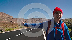 Traveler woman hitchhiking on a sunny road and walking. Backpacker woman looking for a ride to start a journey on a