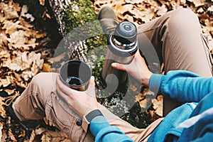 Traveler woman holding a cup of tea and thermos in autumn forest