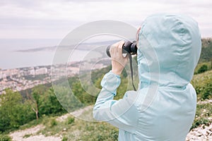 Traveler woman looking through binoculars on sea bay.