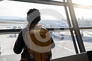 Traveler woman plan and backpack see airplane flight at the airport glass window