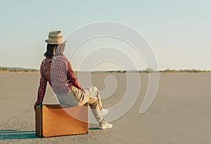 Traveler woman sitting on suitcase on road, copy-space