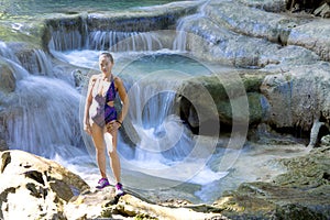 Traveler woman in swimsuit enjoy on stone at Erawan Waterfall