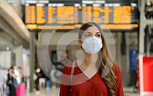 Traveler woman wearing KN95 FFP2 face mask at train station to protect from virus and smog. Young caucasian woman with timetables