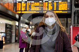 Traveler woman wearing medical face mask at the airport. Happy young woman walking and looking up with behind timetables of