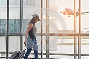 Traveler women plan and backpack see the airplane at the airport glass window, girl tourist hold bag and waiting near luggage in h