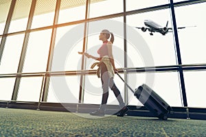 Traveler women plan and backpack see the airplane at the airport glass window, girl tourist hold bag and waiting near luggage in h