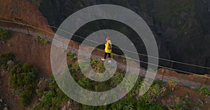 A traveler in a yellow jacket, hat and backpack walks on a paradise island. Active young woman climbs on top of cliff