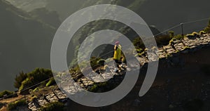 A traveler in a yellow jacket, hat and backpack walks on a paradise island. Active young woman climbs on top of cliff