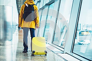 Traveler with yellow suitcase backpack at airport on background large window blue sky, passenger waiting flight in departure loung