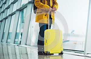 Traveler with yellow suitcase backpack at airport on background window blue sky, passenger waiting flight in departure lounge