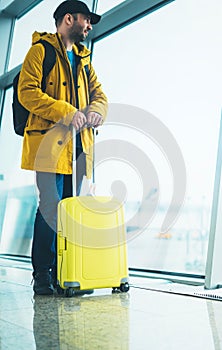 Traveler with yellow suitcase backpack at airport on background window blue sky, passenger waiting flight in departure lounge area