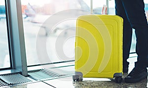 Traveler with yellow suitcase backpack at airport on background window blue sky, passenger waiting flight in departure lounge area