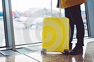 Traveler with yellow suitcase backpack at airport on background window blue sky, passenger waiting flight in departure lounge area