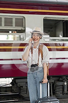 Traveler young asian woman talking on cell phone at terminal train station. Happy tourist travel by train. woman