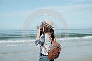 traveler young woman in casual dress holding camera and take photo with backpack stand alone on beach has sea background