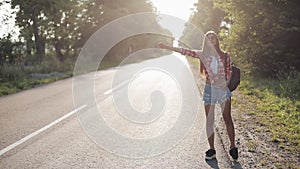 Traveler young woman hitchhiking on a sunny road. Young girl looking for a ride to start a journey. Summer time