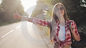 Traveler young woman hitchhiking on a sunny road. Young girl looking for a ride to start a journey. Summer time