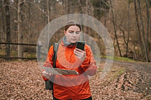 Traveler young woman searching direction with a map in the forest. Young lost girl in sports clothes with a map in her