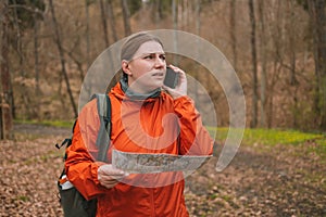 Traveler young woman searching direction with a map in the forest. Young lost girl in sports clothes with a map in her