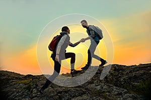 Travelers Hiking in the Mountains at Sunset. Man Helping Woman to Climb to the Top. Family Travel and Adventure.