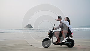 Travelers ride motorbike along sandy sea beach at dusk. Man, woman drive motorcycle on tropical island coastline