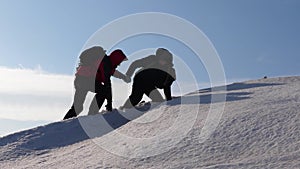 Travelers rise hand in hand to victory through the snow uphill in high winds. tourists in winter work together as team