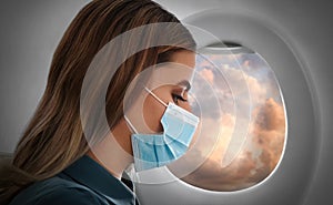 Traveling by airplane during coronavirus pandemic. Woman with face mask near porthole