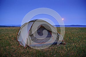 Traveling and camping concept - summer landscape and tent, twilight, moon on dark sky with stars. Beautiful nature - field, forest