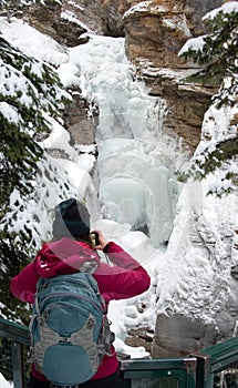 Traveling Canada, woman takes pictures of Johnston Canyon Waterfall - Frozen Lower Falls with turquoise pool below Banff National