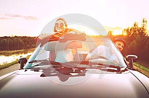 Traveling by car - couple in love go by cabriolet car in sunset