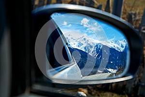 Traveling by car. A photo of a car rearview mirror with a reflection of the road and snow-covered mountains in it