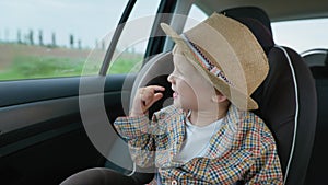 Traveling children, an attractive little male child enjoying ride in car seat and looking out window during summer car