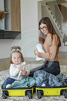 Traveling with children. Happy young mother with little toddler kid packs clothes in suitcase