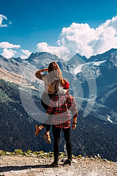 A traveling couple in plaid shirts against the backdrop of mountains. Two tourists on the top of the mountain.
