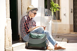 Traveling man sitting on sidewalk reading map