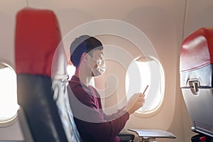 Traveling man wearing protective mask onboard in the aircraft using smartphone, travel under Covid-19 pandemic, safety travels,