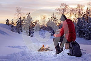 Traveling man in winterwear sitting near fire and having hot drinks.